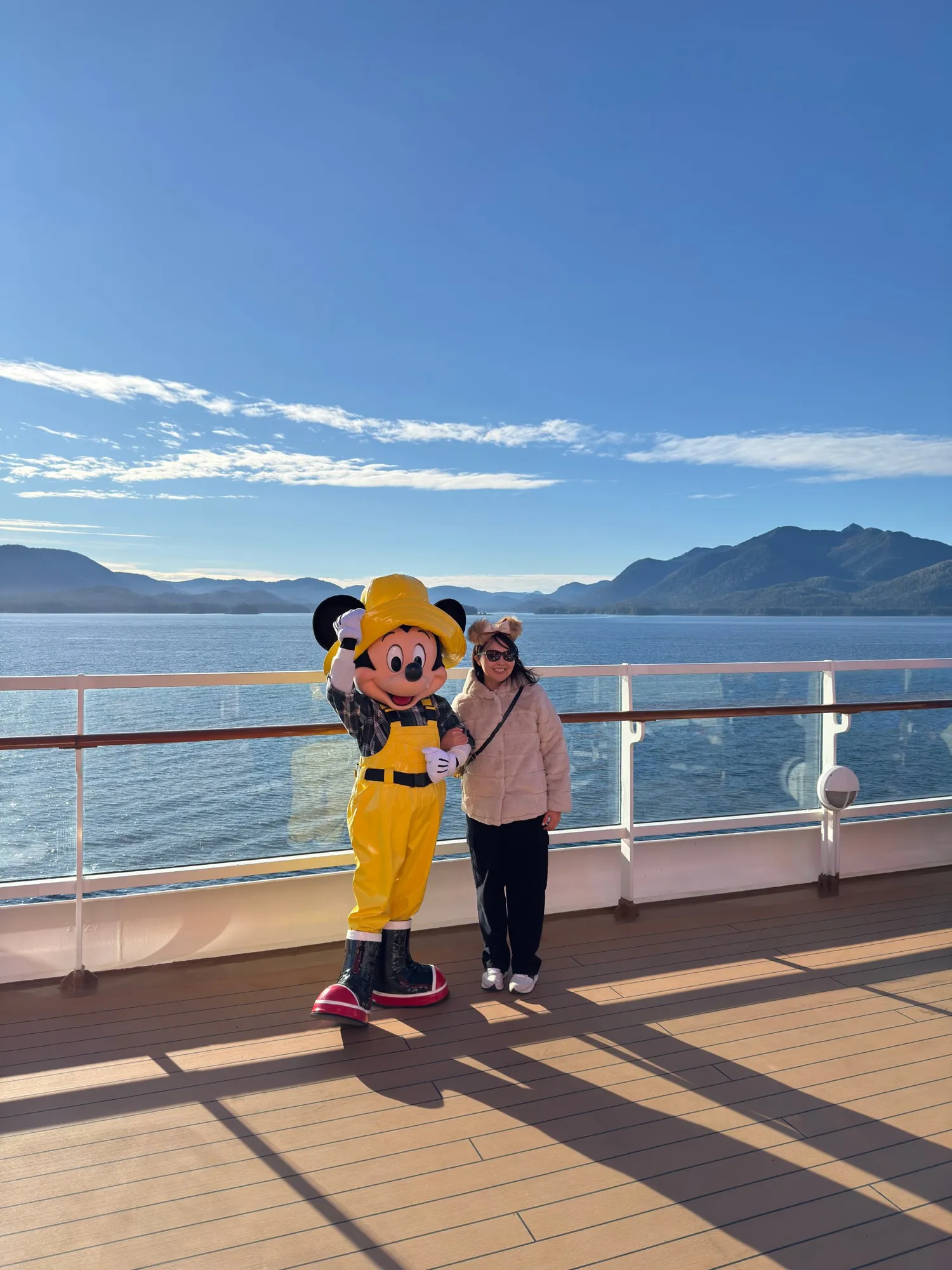 Mickey Mouse in a yellow rain hat and overalls posing with Tomo on the deck of the Disney Wonder in Alaska