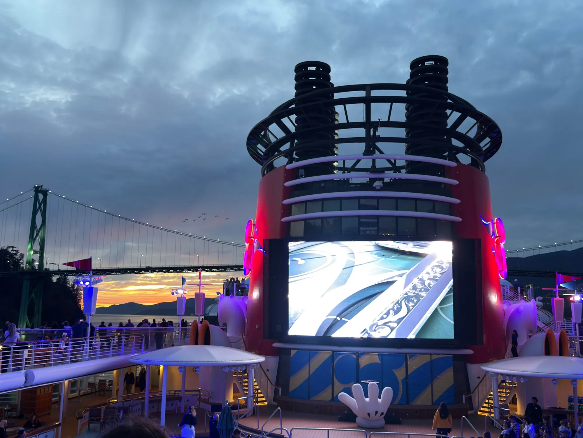 Disney Wonder's Mickey funnel lit up as the ship passes the Lions Gate Bridge at sunset leaving Vancouver
